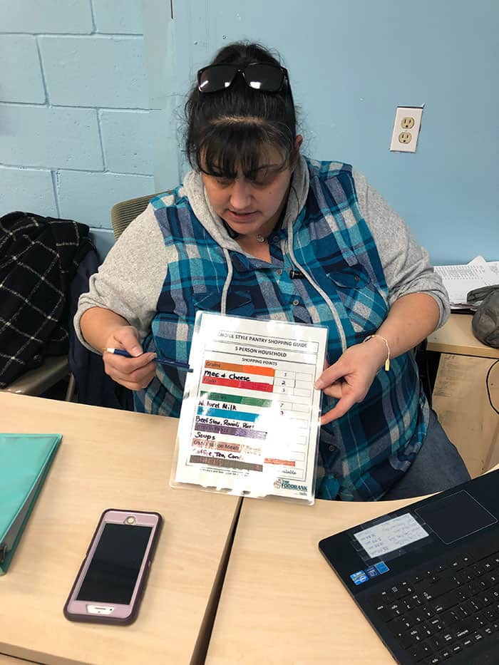 Sustainability manager Lidia Kelly, who is in charge of the food bank, is holding a placard that shows the amount of food available monthly to a 5-person household. (Photo by Judy Smestad-Nunn)