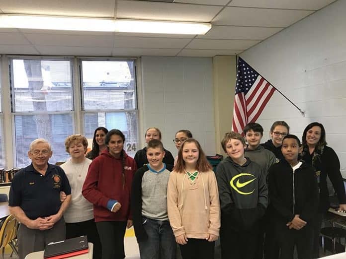 Dina Nagy’s sixth grade class poses beneath their new flag with Bob and Darlene Scheiderman and Superintendent Loren Fuhring. (Photo by Chris Lundy)