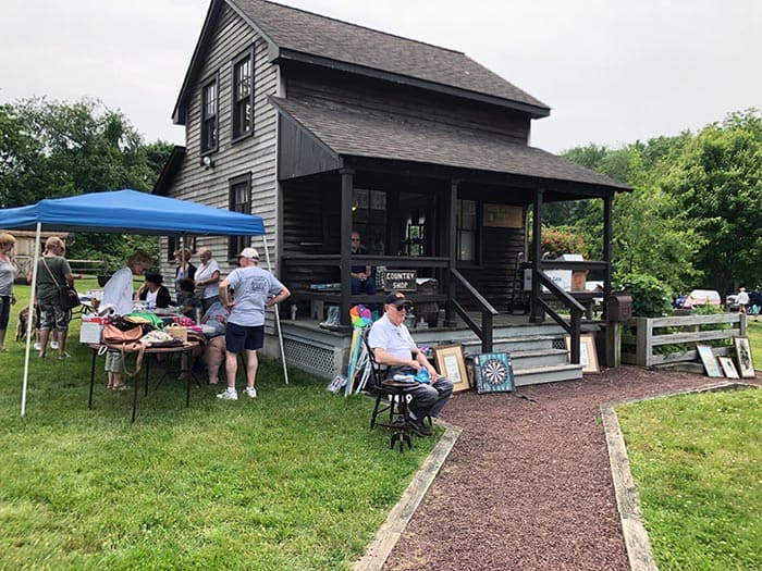 Historical Society President Ed Mangold sells memberships in front of the Lizzie Herbert House, a "country shop" located next to the homestead. (Photo by Judy Smestad-Nunn)