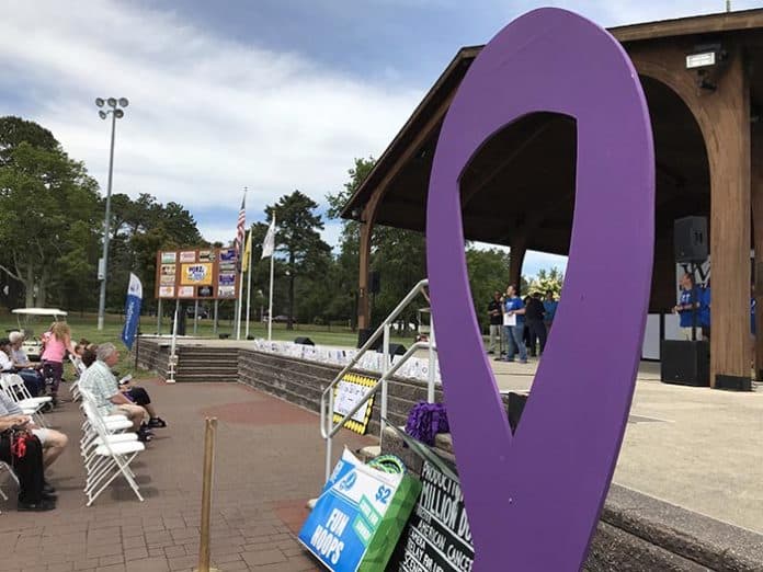 Roxanne Stephens, event leader, speaks from the stage during the welcoming ceremony, framed by the purple ribbon. (Photo by Chris Lundy)